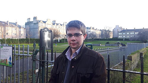 Councillor Jack Caldwell in front of a graffitied sign in Dalmeny Street Park