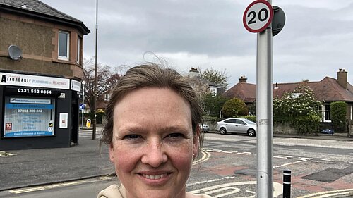 Sanne standing in front of a 20 miles per hour sign at a road junction.