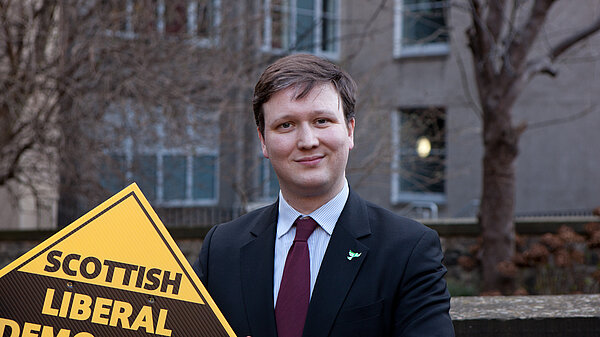 Charles Dundas holding a Lib Dem poster with flats in the background
