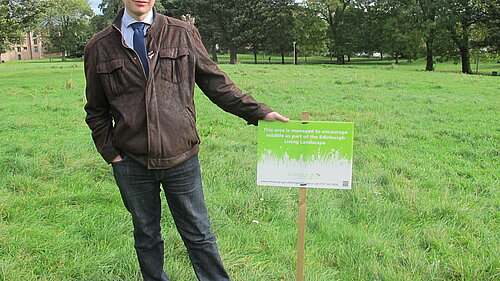 Jack Caldwell standing next to a sign in Pilrig Park that reads "this area is managed to encourage wildlife".